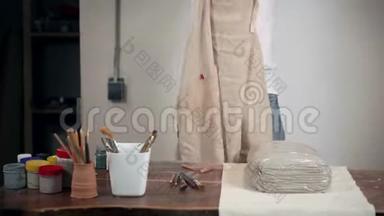 女人正在她的手工作坊里穿上围裙，站在桌子旁边，